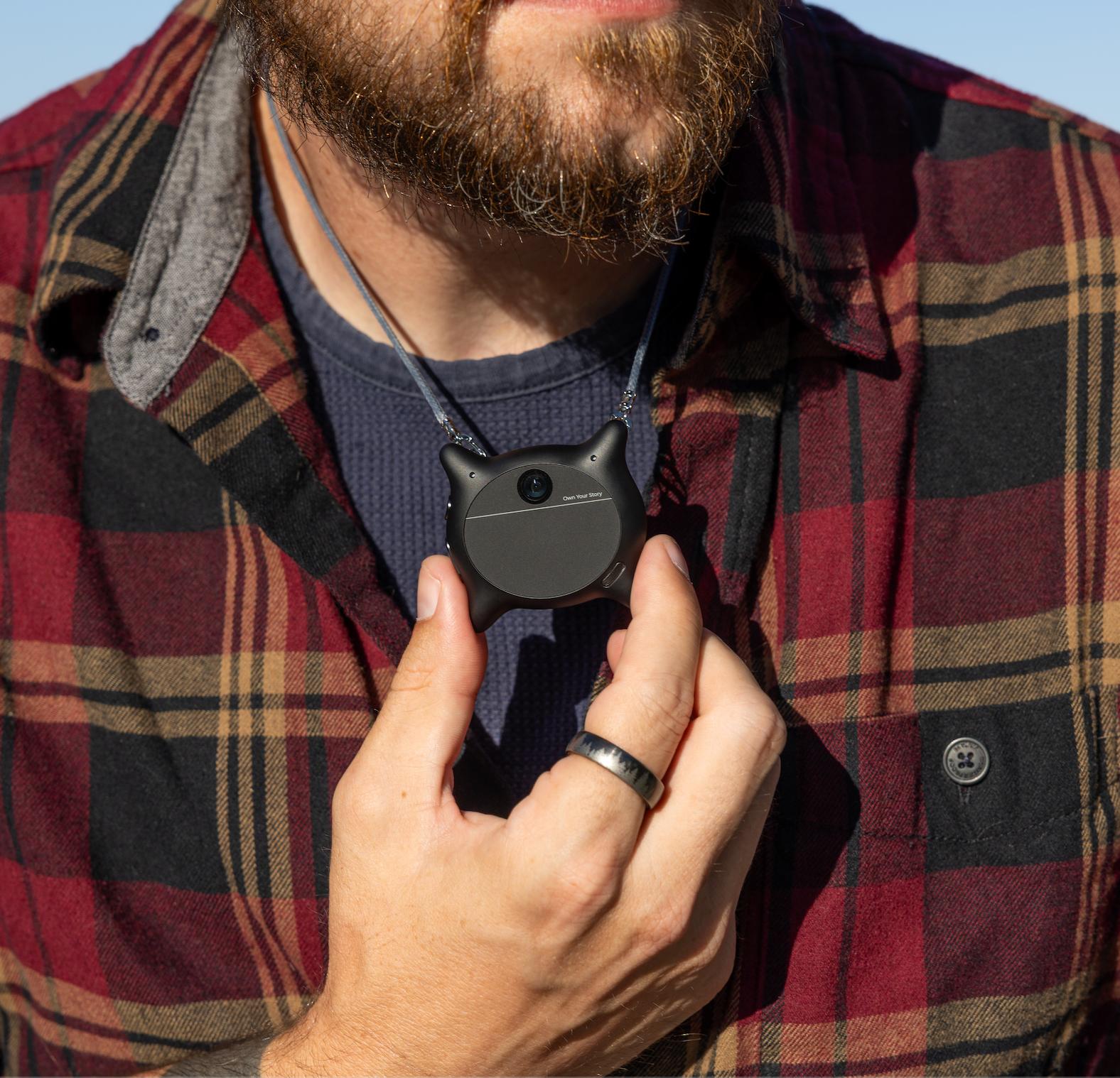 Man wearing and holding a black Looki L1 AI wearable camera as a pendant.